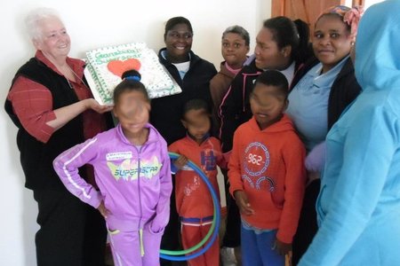 â€˜n Deel van die kinders in die Gansbaai Huis wat nie kon wag vir die koek om gesny te word nie, met Joanne Swart wat Gansbaai Superspar se koek houvas. Die kinders se gesiggies word op die foto's verskuil om hul identitiet te beskerm.